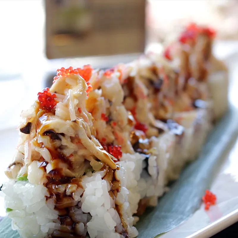 Sushi rolls topped with crab salad, roe, and dark sauce.