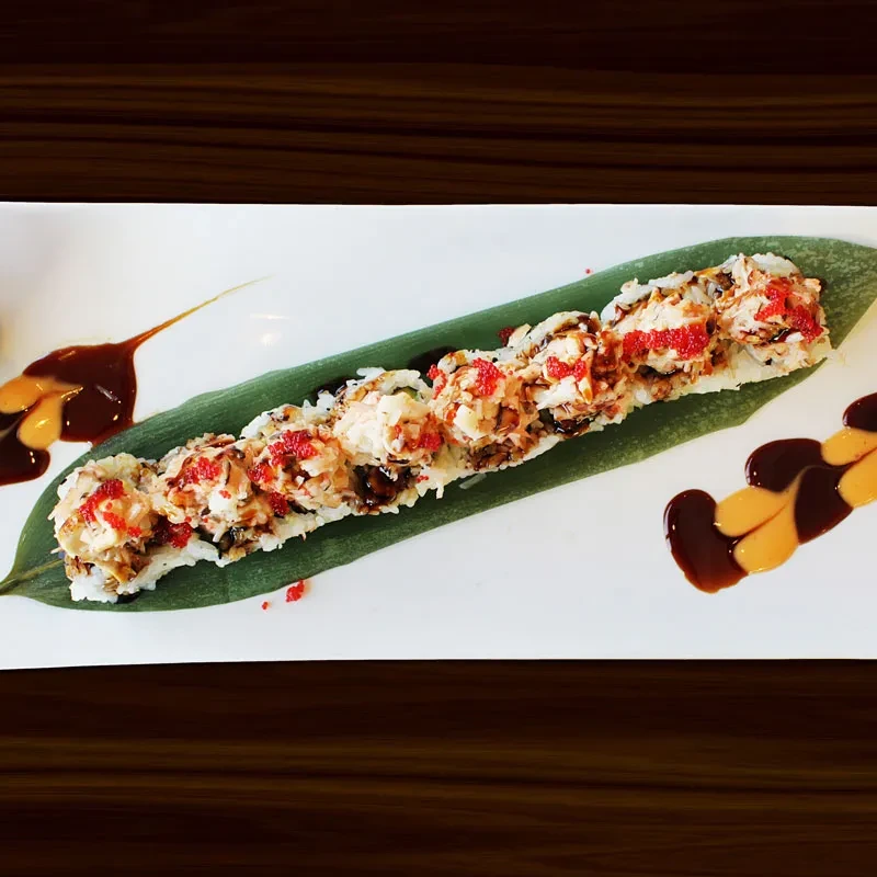 Sushi roll with crab, roe, and sauce on a banana leaf.