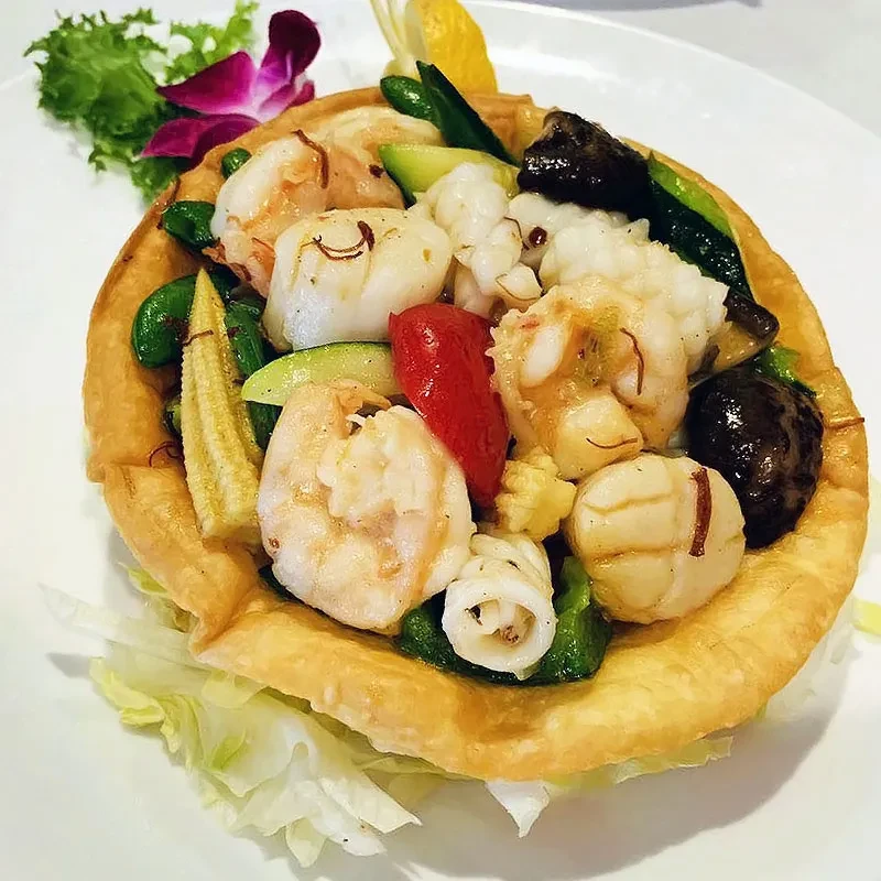 Seafood stir-fry in a fried noodle bowl, garnished with orchid.
