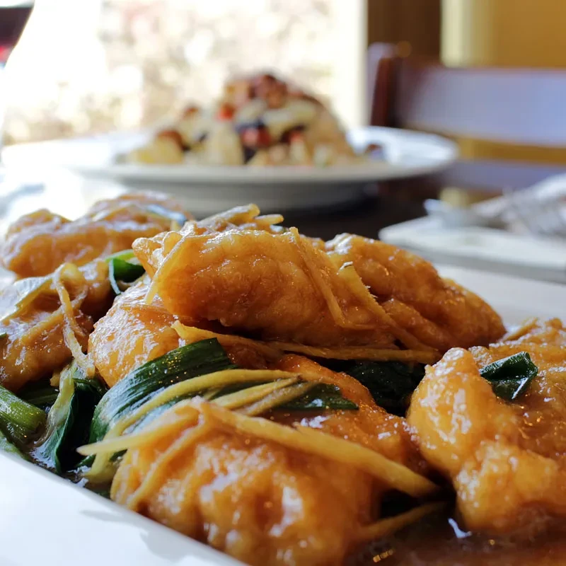A plate of glazed fried dumplings with green onions and ginger.