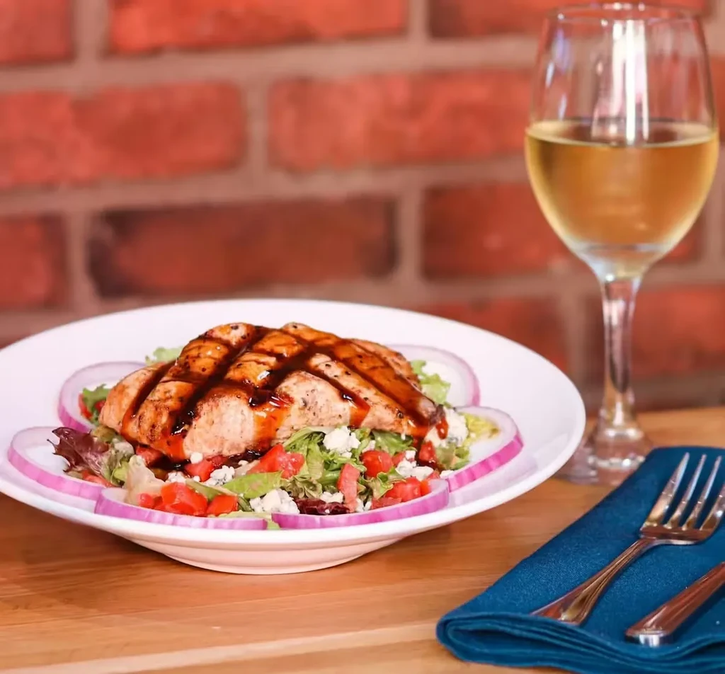 Grilled salmon with dark glaze, mixed salad, white wine on table.