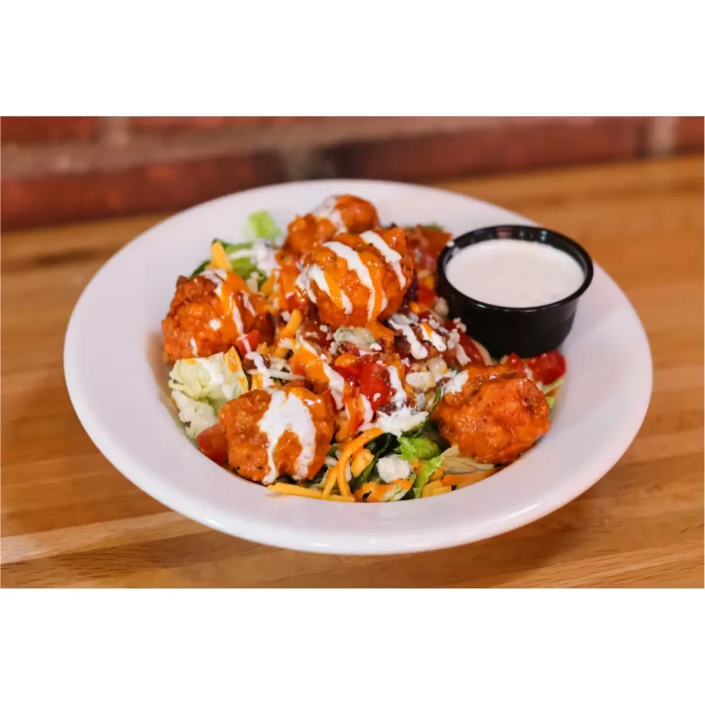 Close-up: Buffalo chicken salad with lettuce, cheese, tomatoes, and white dressing.
