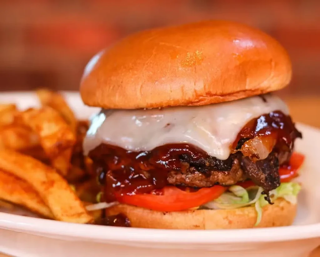 Gourmet burger with melted cheese, caramelized onions, lettuce, and blurred fries.