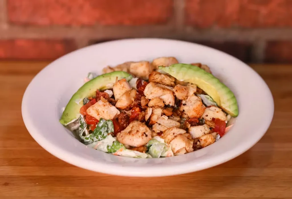 Close-up of chicken, avocado, tomato, and green salad with creamy dressing.