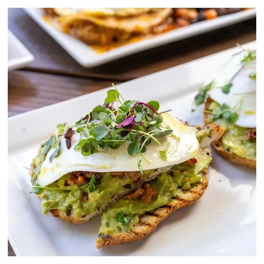 Grilled avocado toast topped with fried egg, crispy bits, and microgreens.