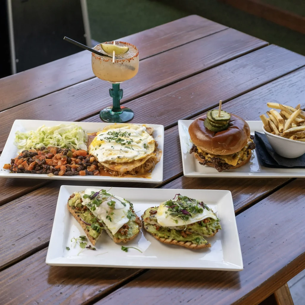 Three distinct food dishes and a cocktail on a wooden table.