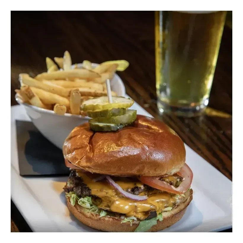 Close-up of stacked cheeseburger with pickles, fries, and beer.