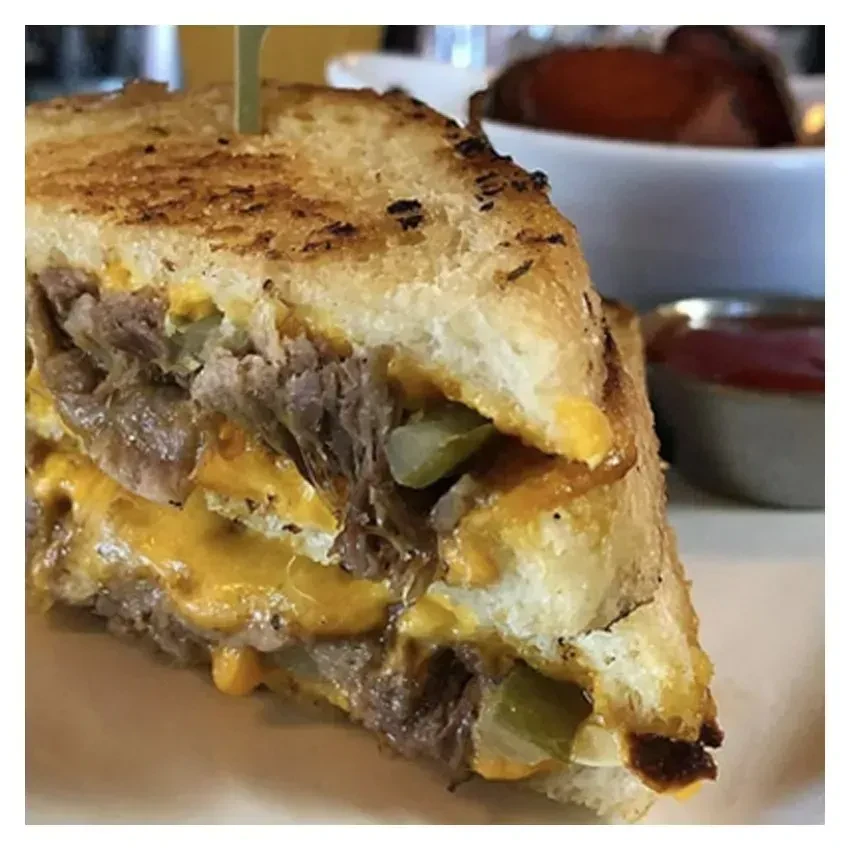 Toasted sandwich with melted cheese, shredded beef, and pickles.