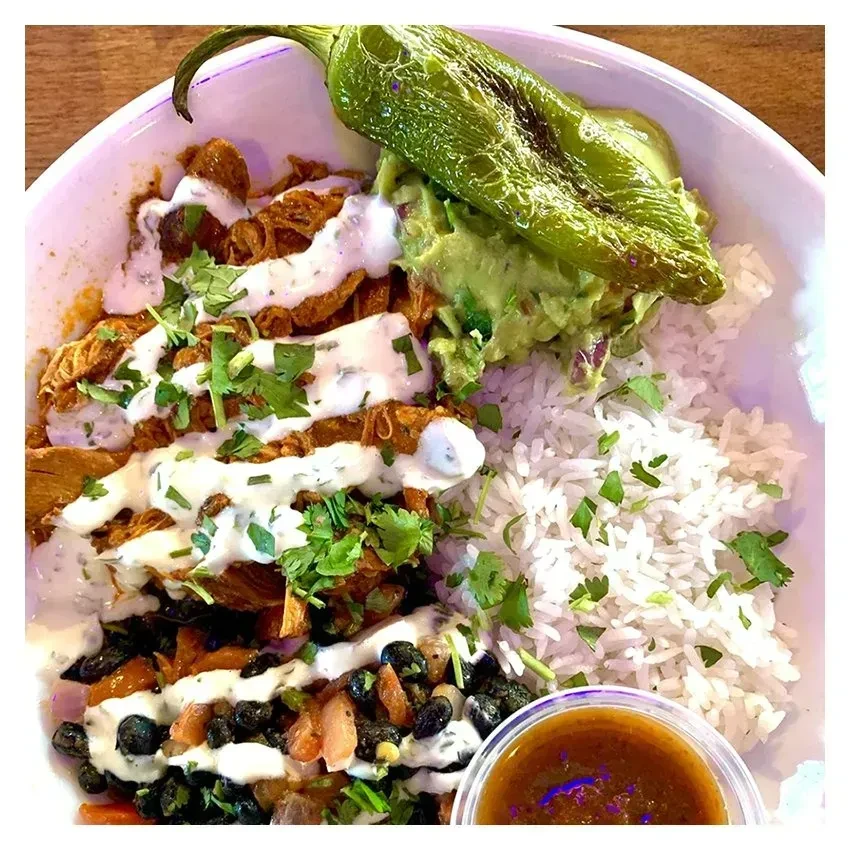 Colorful burrito bowl with meat, rice, beans, guacamole, and pepper.