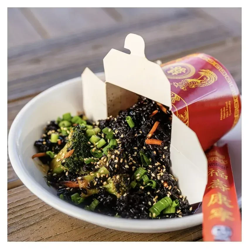 Black rice and vegetables spilling from takeout box into bowl.