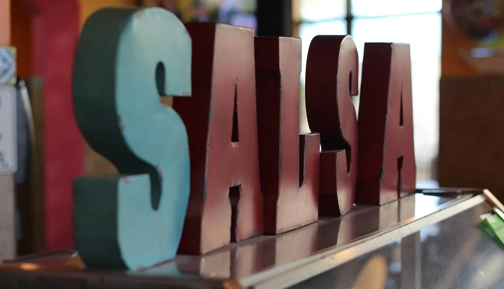 Three-dimensional rustic "SALSA" letters: teal 'S', maroon 'ALSA'.