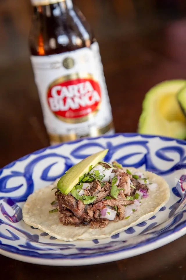 Meat taco with onion, cilantro, avocado on patterned plate.