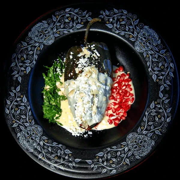 Plated chile relleno with sauce, cheese, herbs, pomegranate, on skull plate.