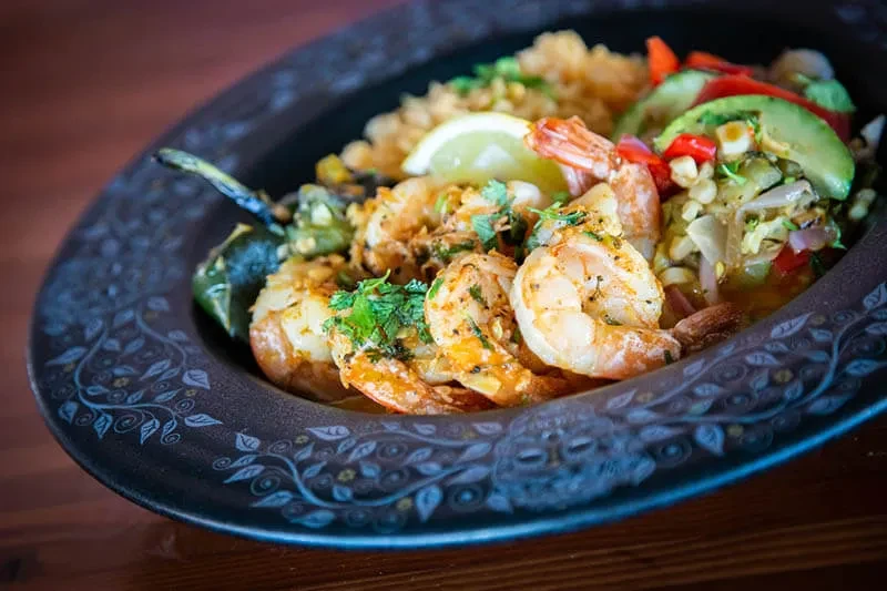 Seasoned shrimp, rice, colorful salad, lime, and chili in an ornate bowl.