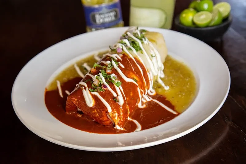 Garnished burrito with red and green sauces and cream on a plate.