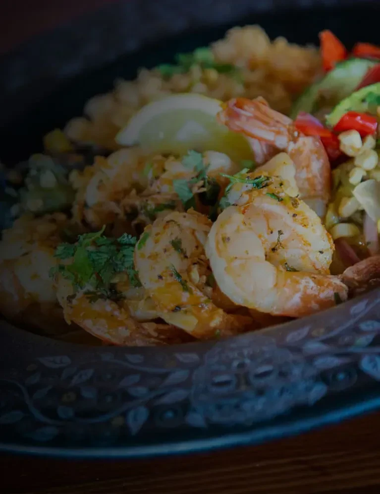Seasoned shrimp, lime, grain, and colorful vegetables in a dark bowl.
