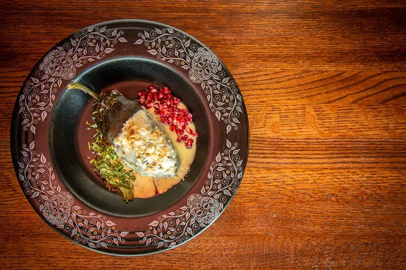 Plated poblano pepper with creamy sauce, nuts, pomegranate, ornate skull plate.
