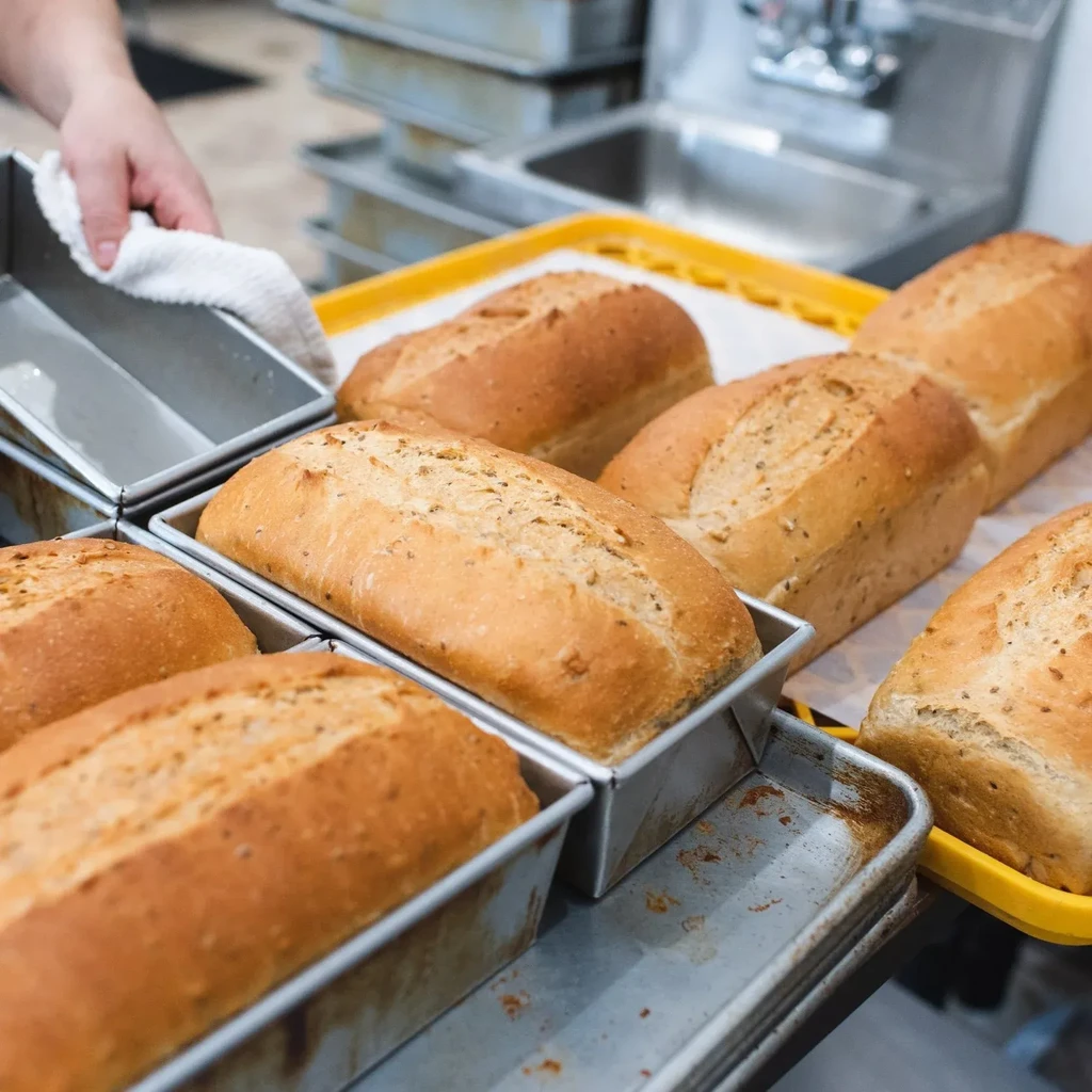 Freshly baked golden-brown bread loaves in pans with a working hand.
