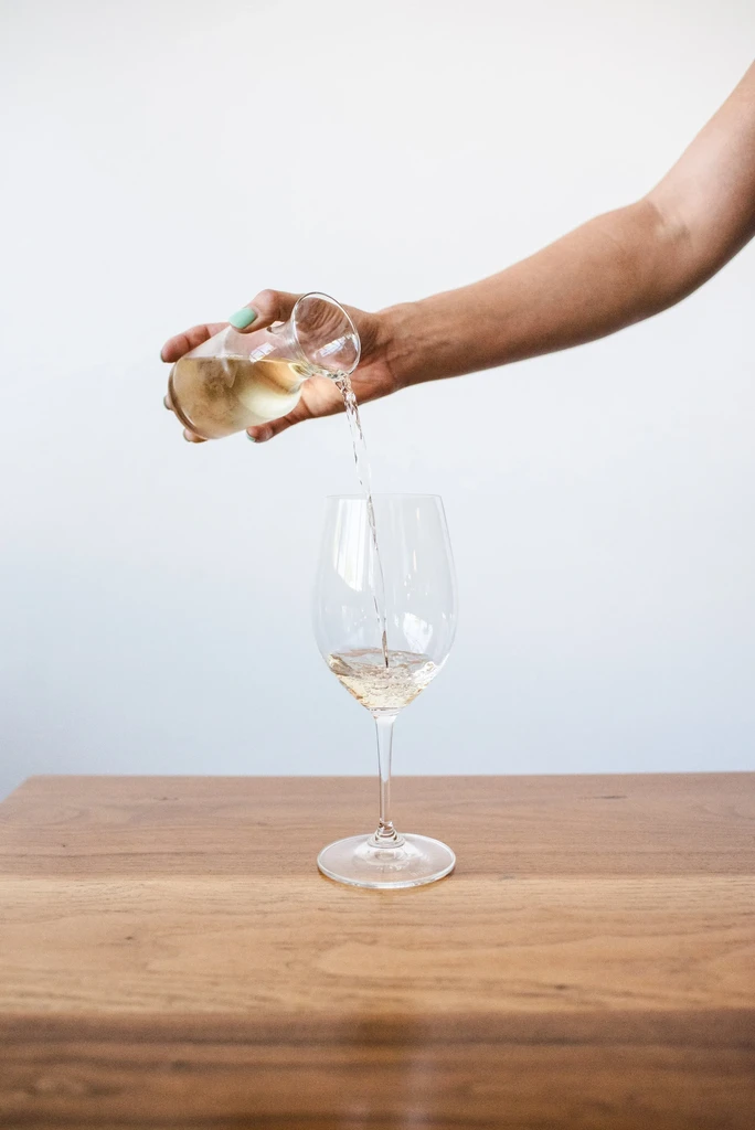 Hand with mint green nails pours white wine into a glass.
