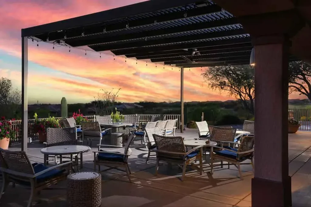 Outdoor patio dining area with wicker chairs, desert, and sunset sky.