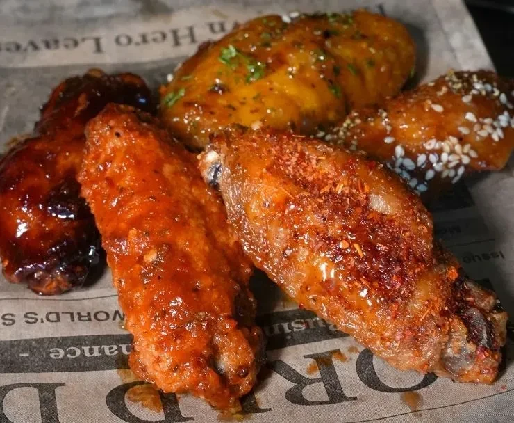 Five seasoned and sauced chicken wings presented on printed paper.
