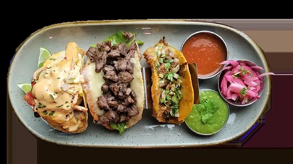 Platter of three distinct tacos with salsa, guacamole, and pickled onions.