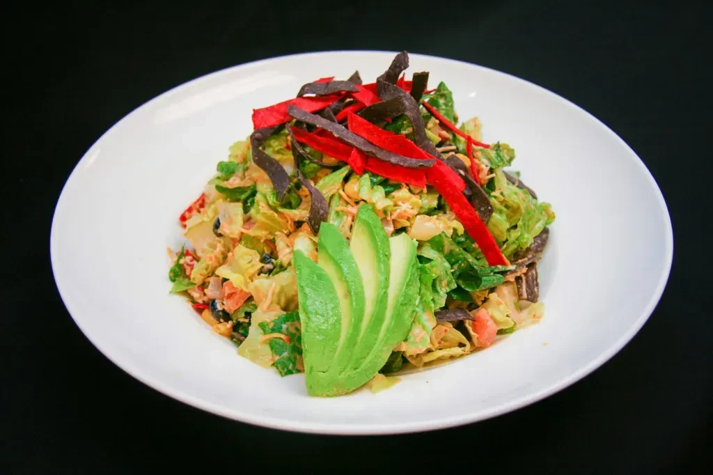 Colorful salad with greens, avocado, red and dark tortilla strips.