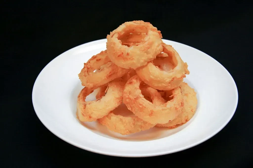 Golden-brown, crispy onion rings stacked on a white plate against black.
