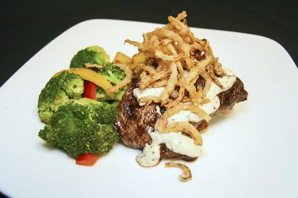 Steak topped with crispy onions, creamy sauce, broccoli, and bell peppers.
