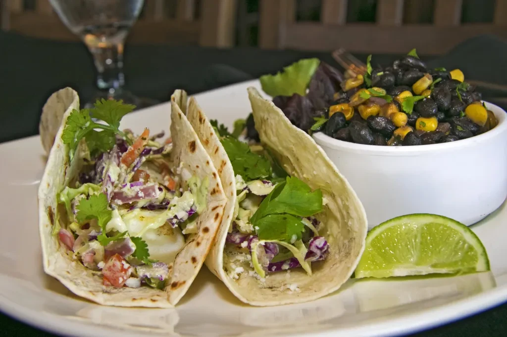 Two soft-shell tacos with colorful slaw, black beans, and lime.