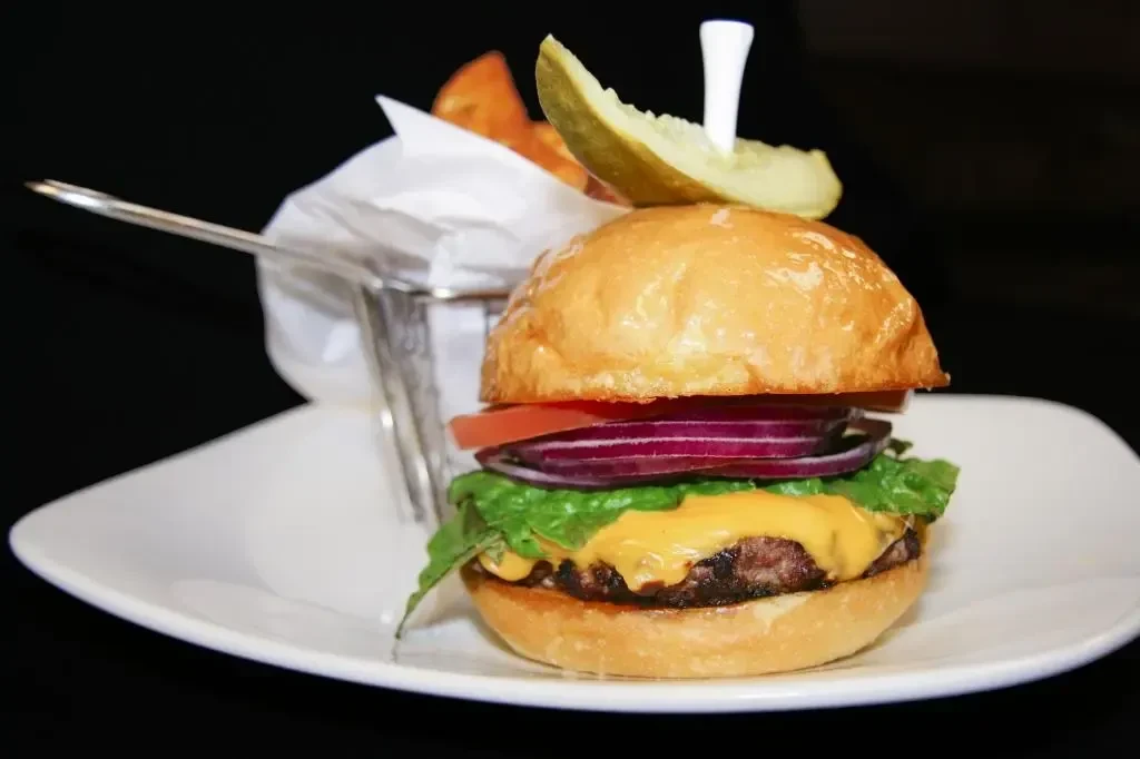 Cheeseburger with cheese, lettuce, tomato, pickle spear, and wedge fries.