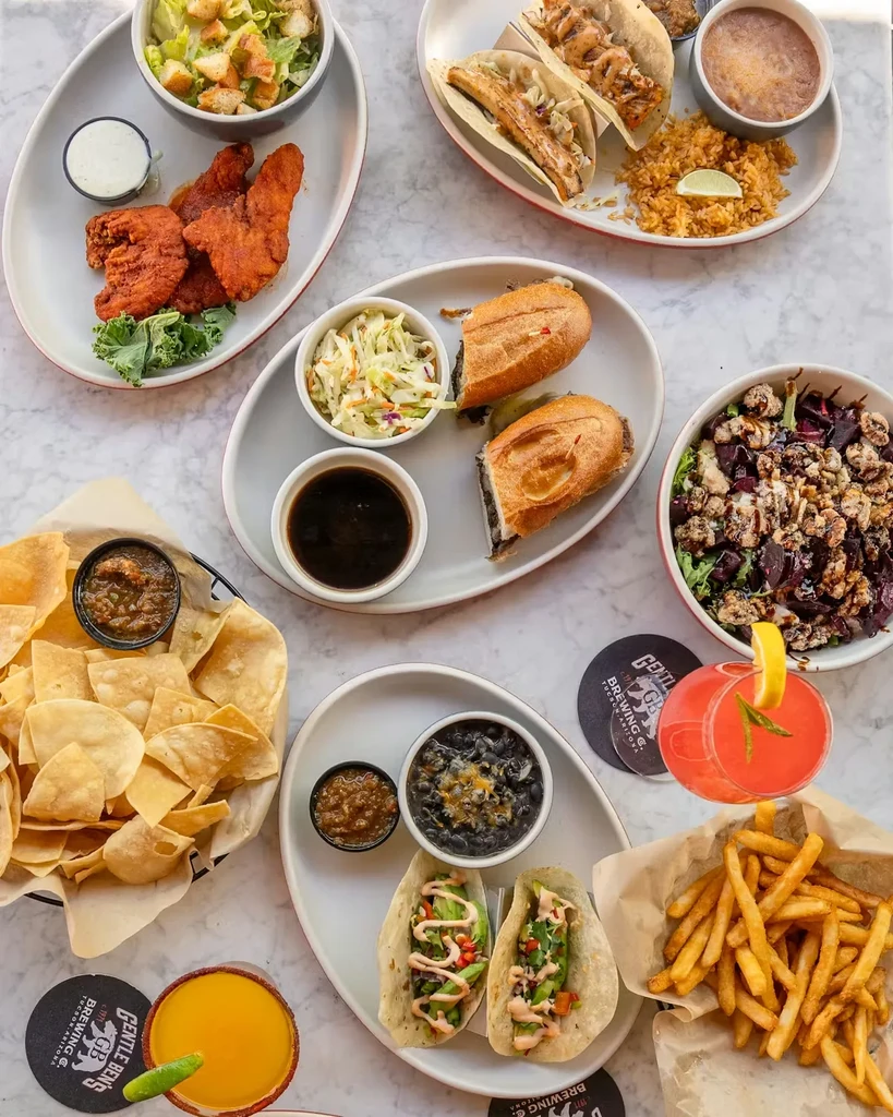 Overhead view of diverse food spread: tacos, chicken, salads, and cocktails.