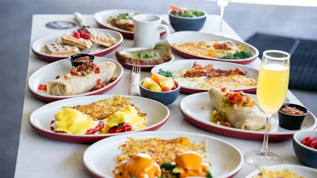 Abundant brunch spread featuring eggs benedict, waffles, burritos, and mimosas.