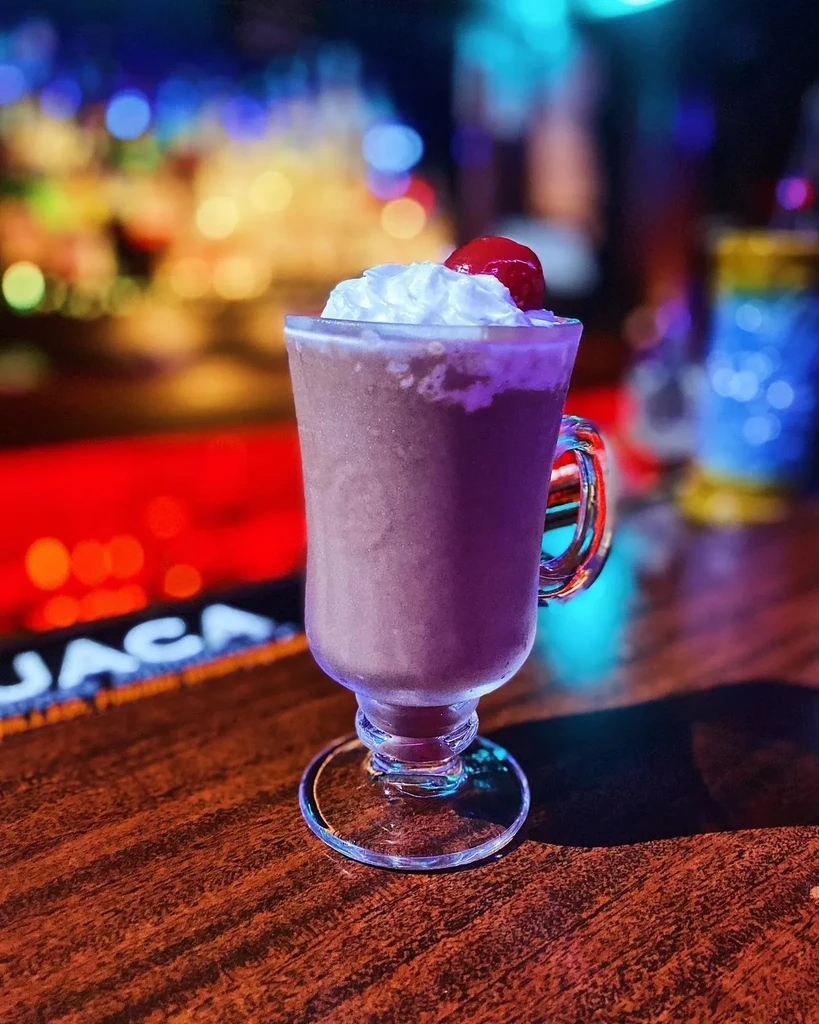 Frosty purple drink with whipped cream, cherry, and blurred bar lights.
