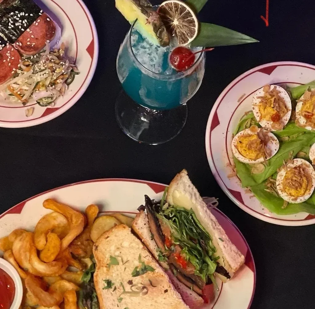 Top-down: Spam musubi, blue cocktail, deviled eggs, and a sandwich meal.