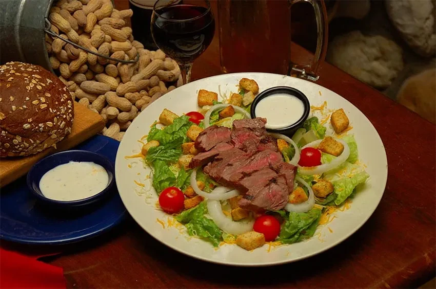 Medium-rare steak salad with bread, dressing, and peanuts on a rustic table.