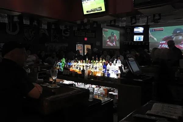 Lively sports bar interior with brightly lit bar and football on screens.