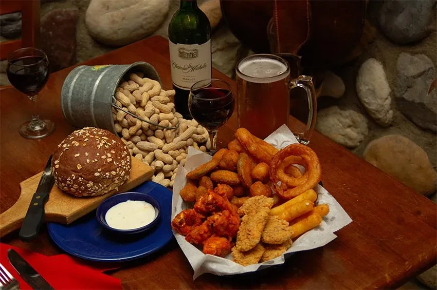 Fried food basket, bread, peanuts, wine, and beer on a rustic table.