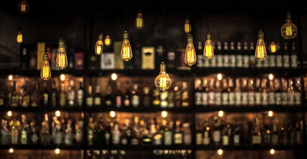 Hanging vintage Edison bulbs illuminate a blurred bar shelf.