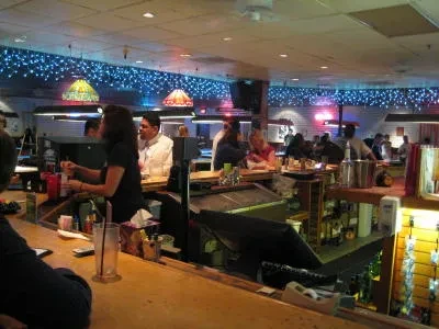 Lively bar scene: bartender, patrons, pool tables, blue string lights.