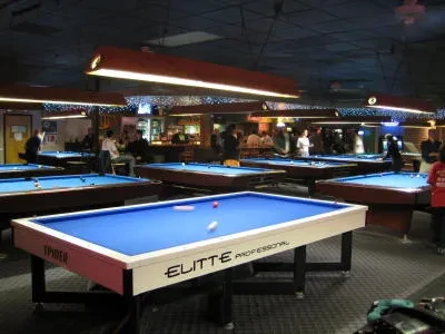 Pool hall interior with blue tables, subdued lighting, and indistinct players.