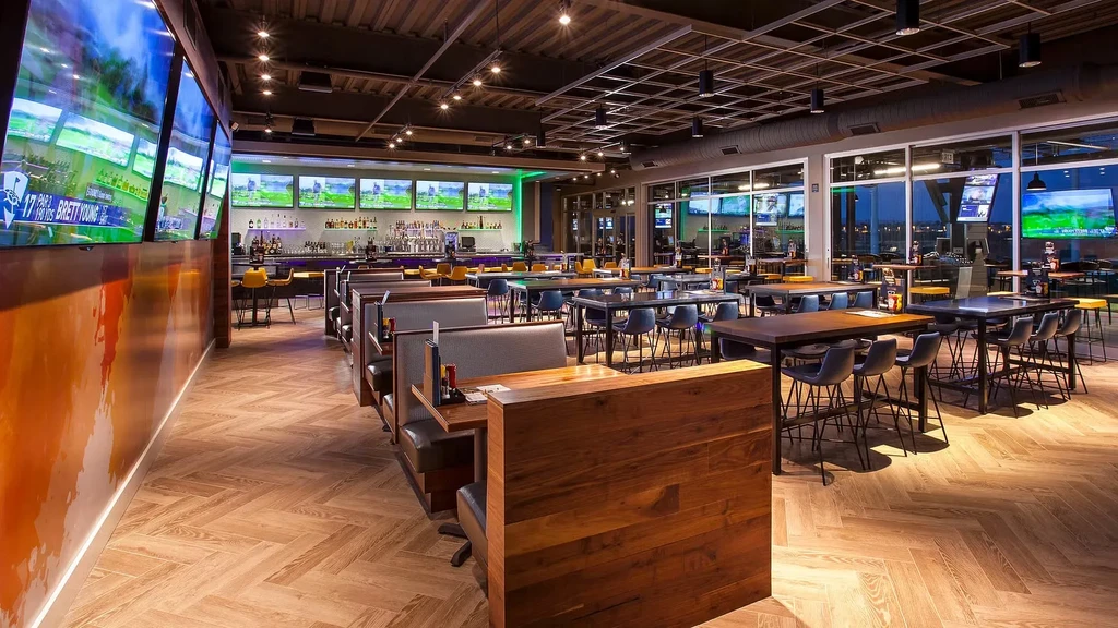 Modern sports bar with illuminated bar, TVs showing golf, and cityscape.