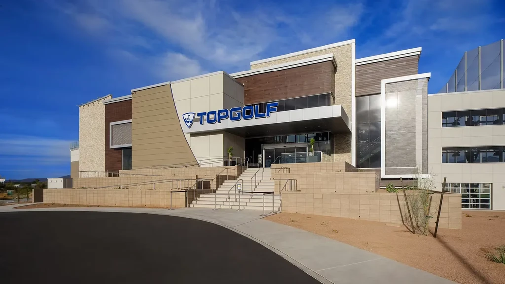 Modern Topgolf facility entrance, grand stairs, under a clear sky.