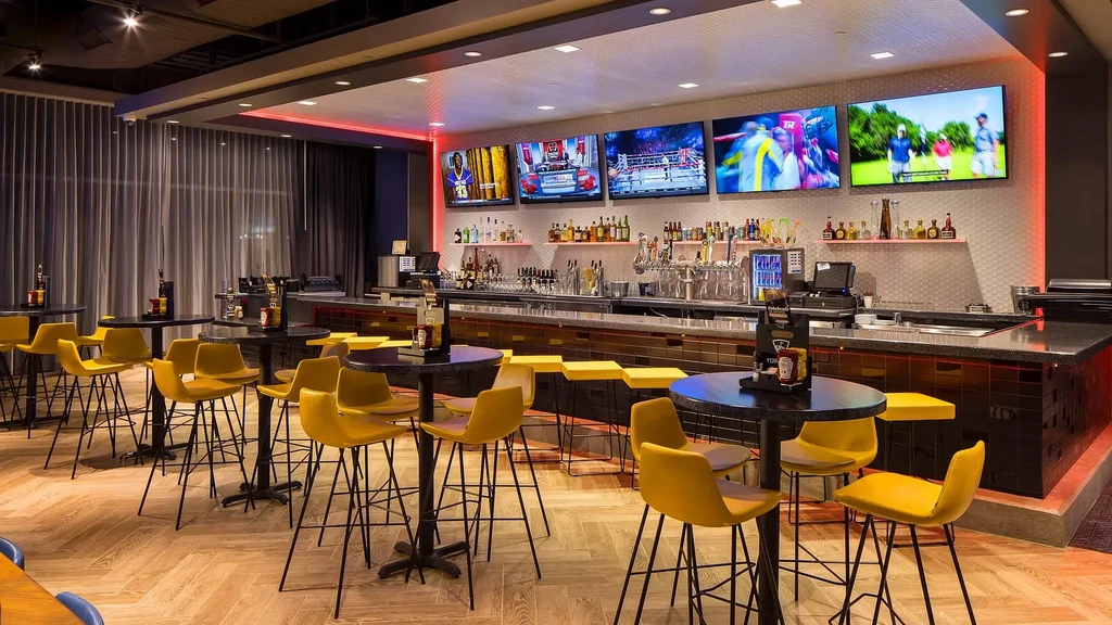 Empty modern bar with five large TVs, red lights, yellow stools.