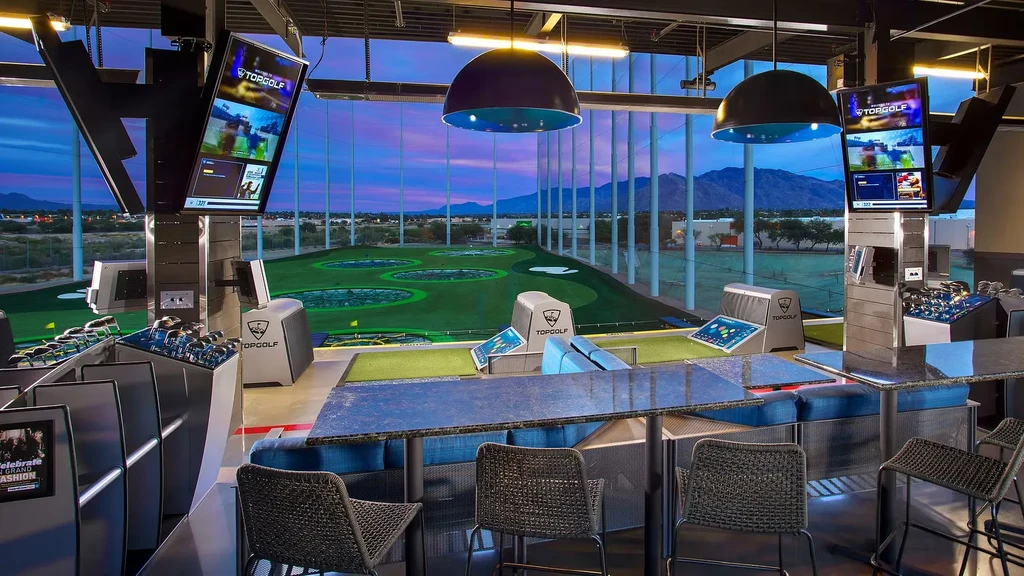 Indoor-outdoor Topgolf golf bays overlook a driving range under twilight sky.