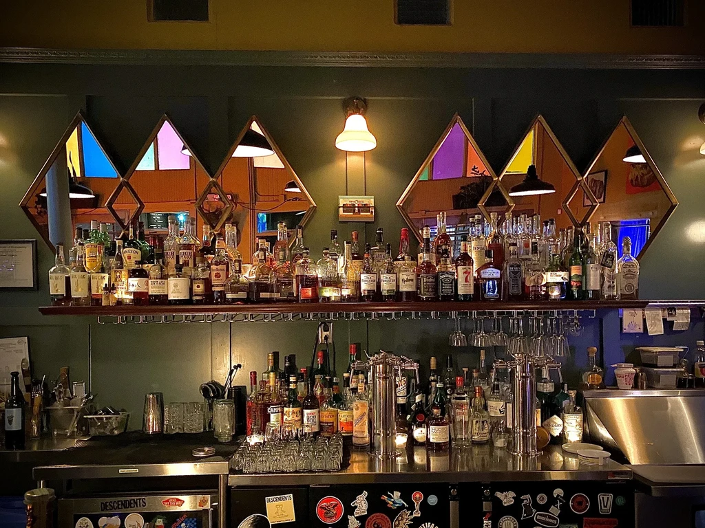 Well-stocked bar with liquor bottles, glassware, and colorful mirrored wall.