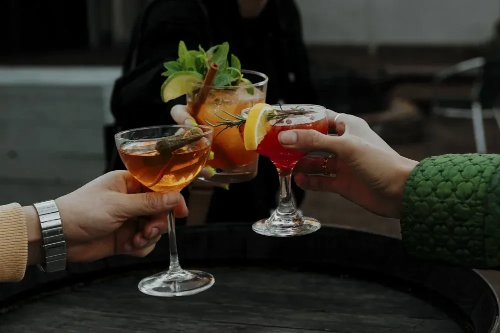 Hands toasting three distinct, garnished cocktails.