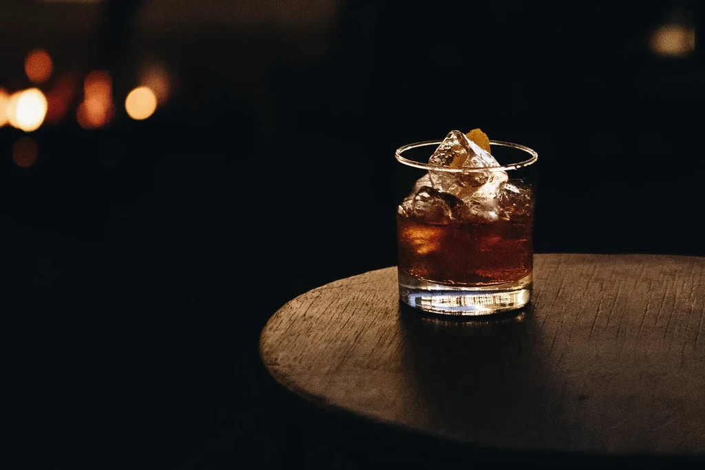 Dark cocktail with ice, citrus peel, on dark wooden table.