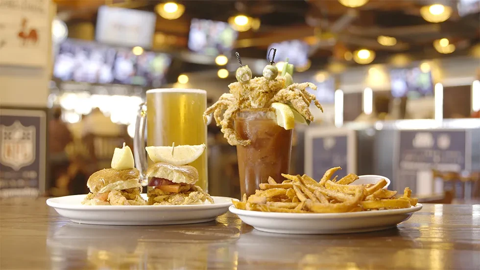 Sliders, beer, a Bloody Mary with fried crab, and fries on a bar.