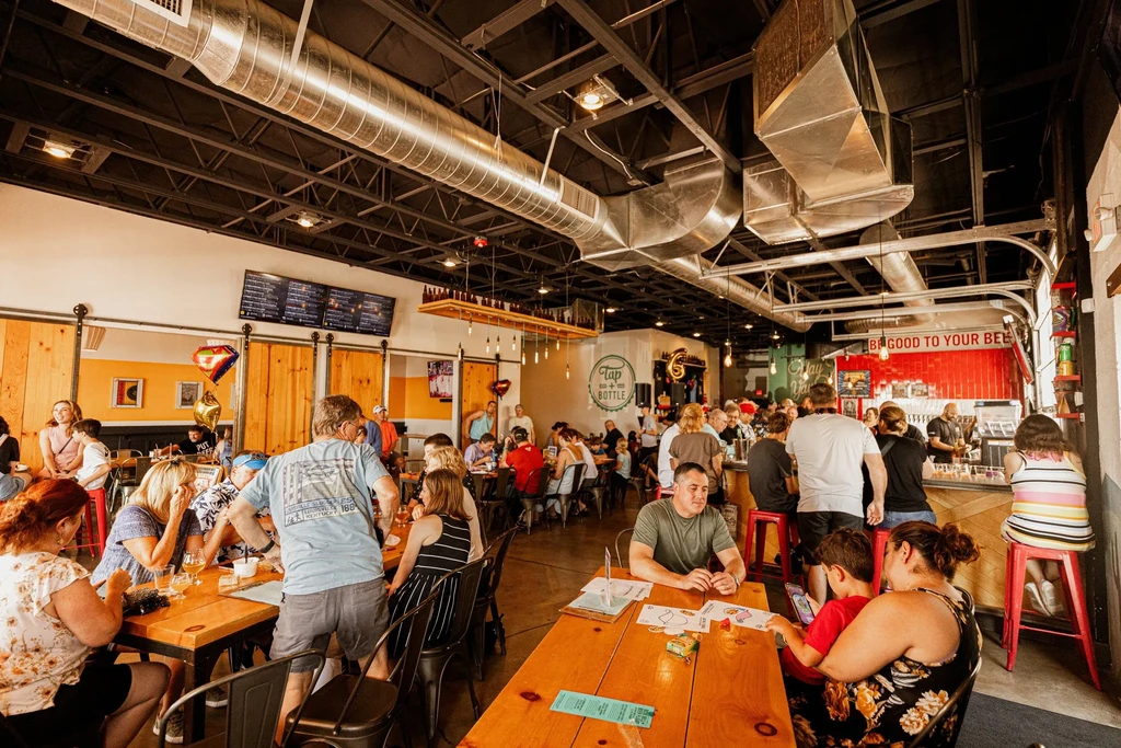 Modern industrial-chic restaurant, bustling with people at tables and bar.